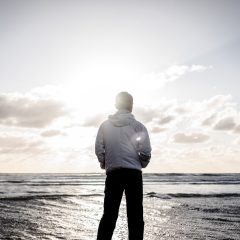 一位穿深色卫衣的技术审校正在双屏工位前调试推流参数，屏幕上显示着编码器状态面板，键盘边贴着几张手写便签